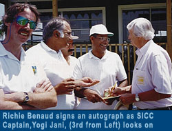 Richie Benaud signs an autograph as SICC captain Yogi Jani, (third from left) looks on